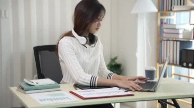 Asyalı bir kadın dizüstü bilgisayar kullanıyor ve hesap makinesi dokümanlarıyla iş raporları yatırım planlarını analiz etmek için merkez büroda çalışıyor.