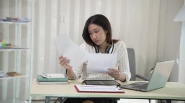 Asyalı bir kadın dizüstü bilgisayar kullanıyor ve hesap makinesi dokümanlarıyla iş raporları yatırım planlarını analiz etmek için merkez büroda çalışıyor.