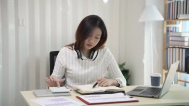 Asyalı bir kadın dizüstü bilgisayar kullanıyor ve hesap makinesi dokümanlarıyla iş raporları yatırım planlarını analiz etmek için merkez büroda çalışıyor.