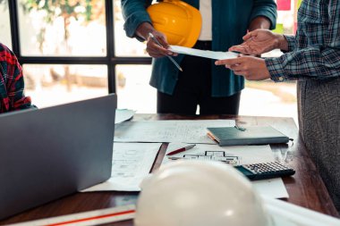 Mühendis ve mimarlardan oluşan bir ekip çalışma, planlama, ölçüm şemaları, inşaat alanındaki binaların planları, ofiste sıkı şapka giyen bir grup profesyonel mühendis.