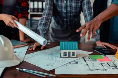 Mühendis ve mimarlardan oluşan bir ekip çalışma, planlama, ölçüm şemaları, inşaat alanındaki binaların planları, ofiste sıkı şapka giyen bir grup profesyonel mühendis.