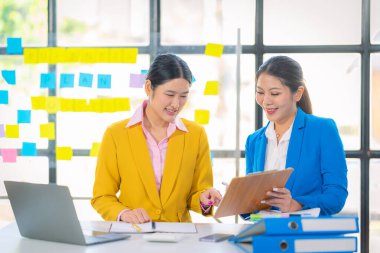 İki Asyalı iş kadını grafikler ve grafiklerle bilgisayar ekranında veri analizi çalışmaları hakkında derin bir tartışma içindeler. Takım çalışmasını göster