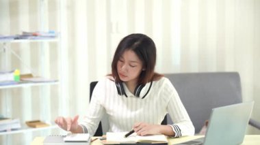 Asyalı bir kadın dizüstü bilgisayar kullanıyor ve hesap makinesi dokümanlarıyla iş raporları yatırım planlarını analiz etmek için merkez büroda çalışıyor.