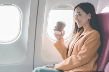 Uçakta bir koltukta oturan Asyalı kadın, uçakla yurtdışına seyahat ederken, seyahatin tadını çıkarırken dengede duruyor..