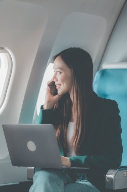 Uçaktaki genç Asyalı kadın, uçak kabininde kıtalararası uçuşlar sırasında internetten film izlerken akıllı telefon kullanıyor. Makinedeki kablosuz bağlantıyı kullanmaktan mutlu.