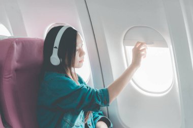Uçakta bir koltukta oturan Asyalı kadın, uçakla yurtdışına seyahat ederken, seyahatin tadını çıkarırken dengede duruyor..