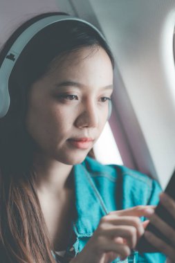 Uçakta bir koltukta oturan Asyalı kadın, uçakla yurtdışına seyahat ederken, seyahatin tadını çıkarırken dengede duruyor..
