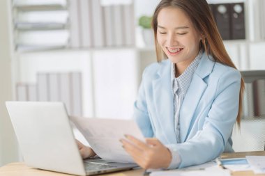 Asyalı iş kadını dijital tablet, hesap makinesi ve dizüstü bilgisayar kullanarak finansal tabloları analiz ediyor borsa verilerini ve iş büyümesini kontrol etmek için geç saatlere kadar çalışıyor.