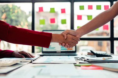 Ofiste siyah takım elbiseli iş adamları el sıkışıyor. İş adamları ve meslektaşları başarılı bir ortaklığı masa ve dizüstü bilgisayar grafikleriyle sıcak bir tokalaşmayla kutluyorlar. Kapat..