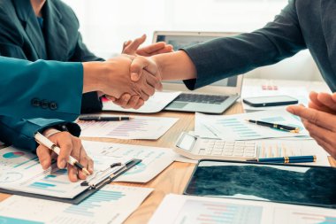 Ofiste siyah takım elbiseli iş adamları el sıkışıyor. İş adamları ve meslektaşları başarılı bir ortaklığı masa ve dizüstü bilgisayar grafikleriyle sıcak bir tokalaşmayla kutluyorlar. Kapat..