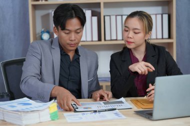 İş ortakları yeni bir proje üzerinde birlikte çalışıyorlar. Toplantıda hesap makinesi kullanarak finansal belgeleri analiz ediyorlar. Çalışma masasında konuşurken, iş problemlerini çözmek için grafik ve grafiklerdeki verileri analiz edin.