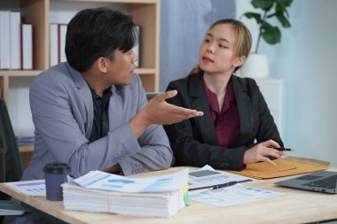 İş ortakları yeni bir proje üzerinde birlikte çalışıyorlar. Toplantıda hesap makinesi kullanarak finansal belgeleri analiz ediyorlar. Çalışma masasında konuşurken, iş problemlerini çözmek için grafik ve grafiklerdeki verileri analiz edin.