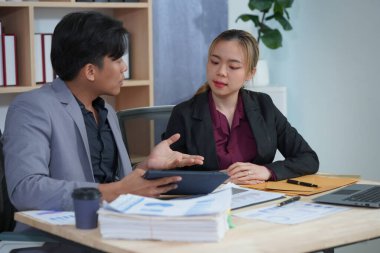 İş ortakları yeni bir proje üzerinde birlikte çalışıyorlar. Toplantıda hesap makinesi kullanarak finansal belgeleri analiz ediyorlar. Çalışma masasında konuşurken, iş problemlerini çözmek için grafik ve grafiklerdeki verileri analiz edin.