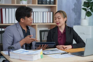 İş ortakları yeni bir proje üzerinde birlikte çalışıyorlar. Toplantıda hesap makinesi kullanarak finansal belgeleri analiz ediyorlar. Çalışma masasında konuşurken, iş problemlerini çözmek için grafik ve grafiklerdeki verileri analiz edin.