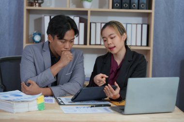 İş ortakları yeni bir proje üzerinde birlikte çalışıyorlar. Toplantıda hesap makinesi kullanarak finansal belgeleri analiz ediyorlar. Çalışma masasında konuşurken, iş problemlerini çözmek için grafik ve grafiklerdeki verileri analiz edin.