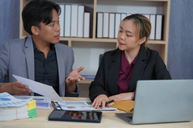 İş ortakları yeni bir proje üzerinde birlikte çalışıyorlar. Toplantıda hesap makinesi kullanarak finansal belgeleri analiz ediyorlar. Çalışma masasında konuşurken, iş problemlerini çözmek için grafik ve grafiklerdeki verileri analiz edin.