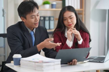 İş ortakları yeni bir proje üzerinde birlikte çalışıyorlar. Toplantıda hesap makinesi kullanarak finansal belgeleri analiz ediyorlar. Çalışma masasında konuşurken, iş problemlerini çözmek için grafik ve grafiklerdeki verileri analiz edin.