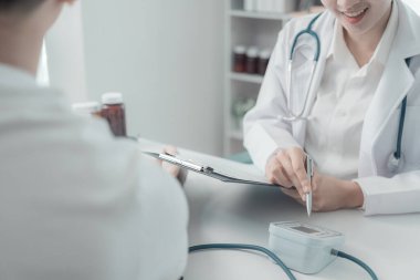 Genç Asyalı hemşire, genç adamın kan basıncını ölçerken masada oturuyorlar, tıbbi sağlık konsepti.