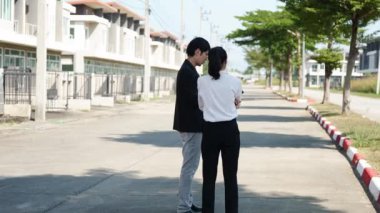 İki Asyalı yatırımcı, bir kadın ve bir erkek, bir köy inşaat projesine gitmek için yürüyorlar. Ev detayları, yeni ev satın alma fikirleri