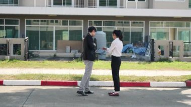 İki Asyalı yatırımcı, bir kadın ve bir erkek, bir köy inşaat projesine gitmek için yürüyorlar. Ev detayları, yeni ev satın alma fikirleri