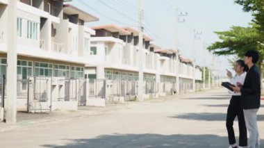 İki Asyalı yatırımcı, bir kadın ve bir erkek, bir köy inşaat projesine gitmek için yürüyorlar. Ev detayları, yeni ev satın alma fikirleri