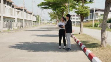 İki Asyalı yatırımcı, bir kadın ve bir erkek, bir köy inşaat projesine gitmek için yürüyorlar. Ev detayları, yeni ev satın alma fikirleri