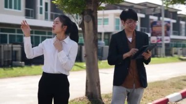 İki Asyalı yatırımcı, bir kadın ve bir erkek, bir köy inşaat projesine gitmek için yürüyorlar. Ev detayları, yeni ev satın alma fikirleri