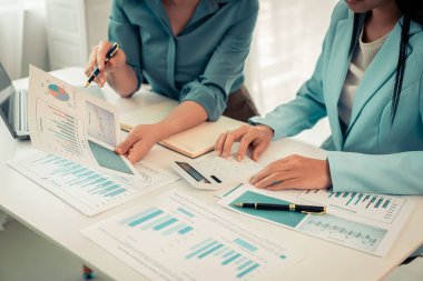 İki Asyalı kadın mali işlem belgelerini inceliyor ve kar ve iş gücünü artırmak için bir iş fikri hesap makinesiyle harcamaları hesaplıyor.