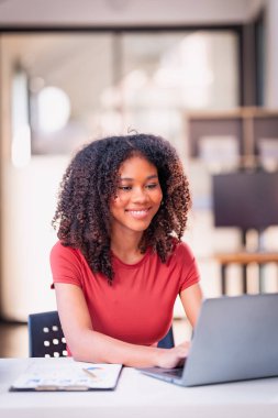 Genç Afrikalı Amerikalı muhasebeci, finans uzmanı ofiste oturuyor ve dizüstü bilgisayar ve belgeler, kontrol listesi ve muhasebe üzerinde çalışıyor..