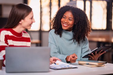 Fazla mesai yapan iki iş kadını ofiste sohbet ediyorlar. Dizüstü bilgisayarlarla, belgelerle, grafiklerle, ofisteki ışıklarla finansal analizlerle çalışıyorlar.