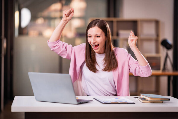 Молодая женщина поднимает руки в победной позе перед ноутбуком и финансовым графиком документ, цель достигнута. Проект завершен