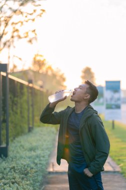 Erkek koşucu spor yaptıktan sonra plastik şişeden su içer, siyah spor giyimli sporcu açık hava eğitimi sırasında suyu tazeler..