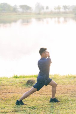 Spor elbiseli genç adam ısınıyor, egzersiz yapıyor, esniyor, sabahları dağın kenarında koşuyor..