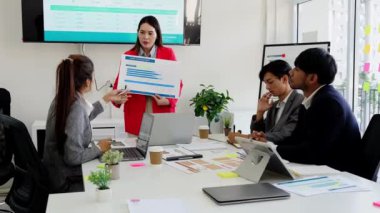 Bir grup genç iş adamı ofiste bir masada oturup kağıt raporlarını ve grafik belgelerini tartışıyor. Fikirleri paylaşın, kararlar verin ve iş sorunlarına beyin fırtınası çözümleri getirin..