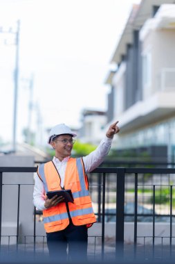 Baş mühendis teslimat için inşa edilen iki katlı ev projesini incelerken bir tablet üzerinde notlar alıyor. dikey resim