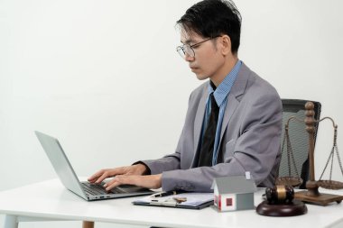 Asyalı erkek yargıç dizüstü bilgisayar, çekiç, konut mahkemesi, aile konutları, iflas hukuku ve ev alımıyla çalışıyor.