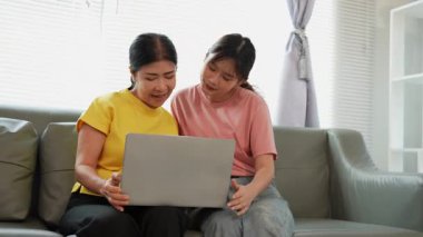 Asyalı anne ve kız kanepede dizüstü bilgisayarda birlikte oynuyorlar, internette bilgi arıyorlar, sosyal medyada geziniyorlar..