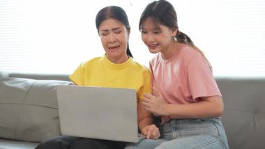 Asyalı anne ve kız kanepede dizüstü bilgisayarda birlikte oynuyorlar, internette bilgi arıyorlar, sosyal medyada geziniyorlar..