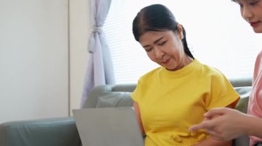 Asyalı anne ve kız kanepede dizüstü bilgisayarda birlikte oynuyorlar, internette bilgi arıyorlar, sosyal medyada geziniyorlar..