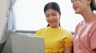 Asyalı anne ve kız kanepede dizüstü bilgisayarda birlikte oynuyorlar, internette bilgi arıyorlar, sosyal medyada geziniyorlar..