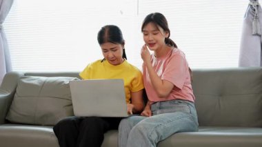 Asyalı anne ve kız kanepede dizüstü bilgisayarda birlikte oynuyorlar, internette bilgi arıyorlar, sosyal medyada geziniyorlar..