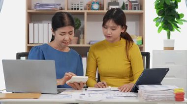 Mutlu Asyalı son sınıf öğrencisi kız ve anne dizüstü bilgisayar kullanarak online bankacılık, borç alma, ev finansmanı.