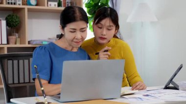 Mutlu Asyalı son sınıf öğrencisi kız ve anne dizüstü bilgisayar kullanarak online bankacılık, borç alma, ev finansmanı.