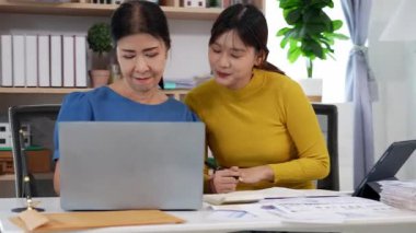 Mutlu Asyalı son sınıf öğrencisi kız ve anne dizüstü bilgisayar kullanarak online bankacılık, borç alma, ev finansmanı.