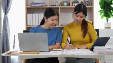 Mutlu Asyalı son sınıf öğrencisi kız ve anne dizüstü bilgisayar kullanarak online bankacılık, borç alma, ev finansmanı.