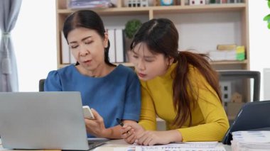 Mutlu Asyalı son sınıf öğrencisi kız ve anne dizüstü bilgisayar kullanarak online bankacılık, borç alma, ev finansmanı.