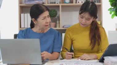 Mutlu Asyalı son sınıf öğrencisi kız ve anne dizüstü bilgisayar kullanarak online bankacılık, borç alma, ev finansmanı.