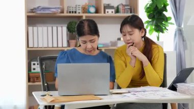 Mutlu Asyalı son sınıf öğrencisi kız ve anne dizüstü bilgisayar kullanarak online bankacılık, borç alma, ev finansmanı.