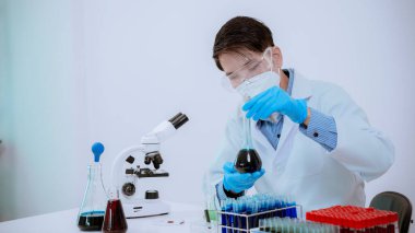 Laboratuvarda çalışan bir bilim adamı mikroskop ile laboratuarda mavi sıvıyla dolu bir test tüpü tutuyor. Muayene. Tıbbi araştırma.