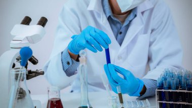 Laboratuvarda çalışan bir bilim adamı mikroskop ile laboratuarda mavi sıvıyla dolu bir test tüpü tutuyor. Muayene. Tıbbi araştırma.